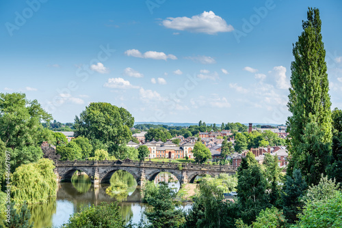 View towards the English bridge, Shrewsbury on a hot July day, with vibrant vegetation and light cloud on a blue sky. England, UK.