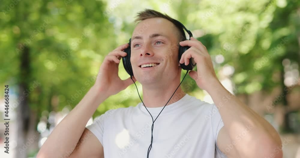 Smiling man puts on big headphones in the summer city, slow motion 4k at 120fps Smiling man puts on big headphones in the summer city, slow motion 4k at 120fps