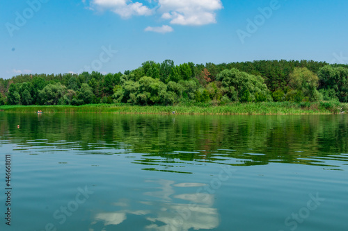Big river Oskol in the east of Ukraine. Beautiful landscape of the river against the background of the forest and the blue sky. White clouds are reflected in the smooth surface of the river.