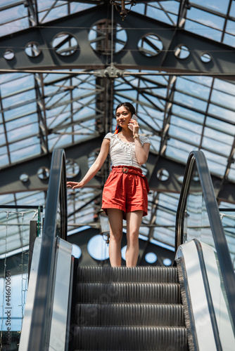 low angle view of stylish asian woman talking on cellphone on escalator