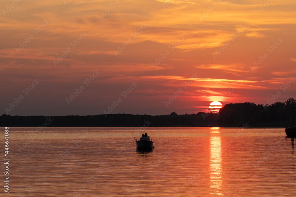 Sunset on the river. Boat with fishermen on the background of a red sunset.