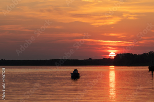 Sunset on the river. Boat with fishermen on the background of a red sunset.