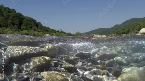 the camera shows the mountains and the bottom of a shallow mountain river