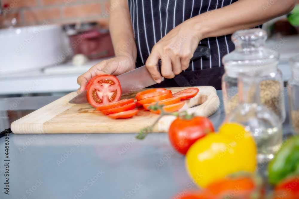 Hand of woman chef slicing tomatoes in luxuly kitchen.