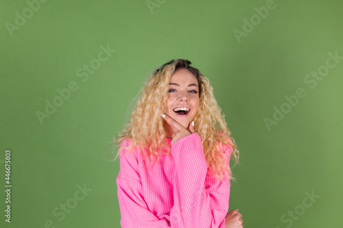 Young blonde woman with long curly hair in pink sweater on green background thoughtful hand on chin look up excited found idea © Анастасия Каргаполов