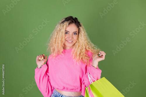 Young blonde woman with long curly hair in pink sweater on green background with colorful paper shopping bags happy cheerful excited © Анастасия Каргаполов