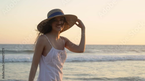 Young long-haired romantic woman in a big hat with fields posing on the shore of the Pacific Ocean at sunset.