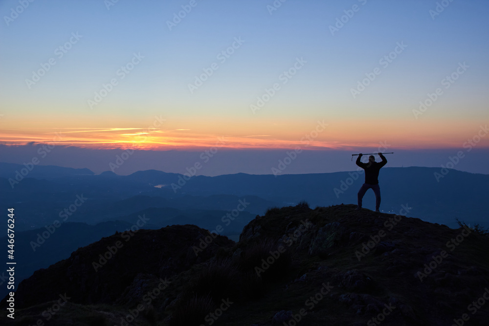 sunset on the mountain, the silhouette of a person on the top of a mountain watches as the sun disappears over the horizon, leaving red and magenta colors