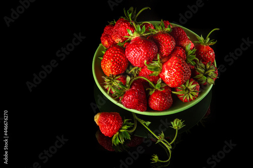 A lot of red ripe strawberries in a plate on a black background. Summer diet and vitamin set idea. Free advertising space