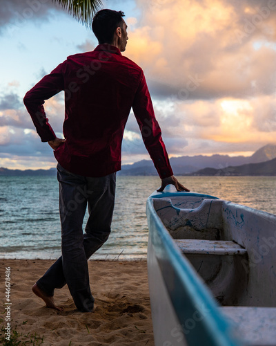 Man standing by canoe in Hawaii on a beach at sunset