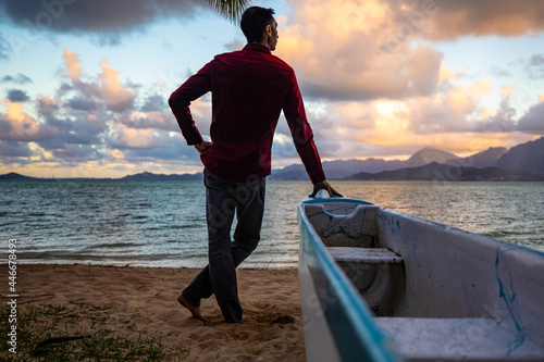 Man standing by canoe in Hawaii on a beach at sunset
