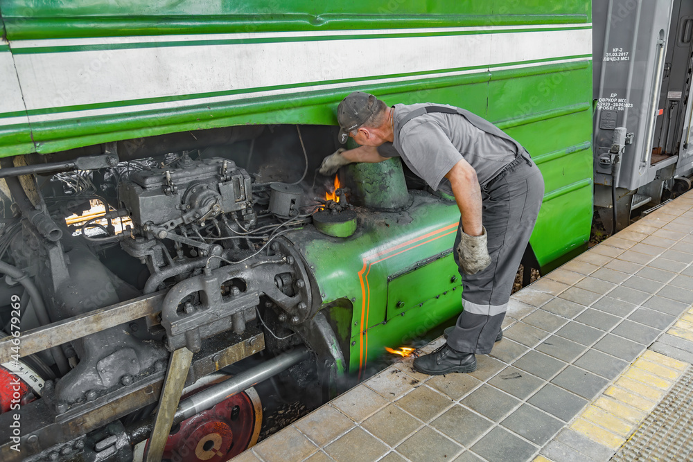 Fototapeta premium Worker extinguishes an ignited green retro steam locomotive on the railway platform of the Pavshino station. Moscow Region, Russia