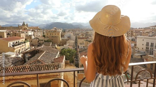 Attractive woman with hat on balcony looks out at cityscape of Palermo, Sicily, Italy photo