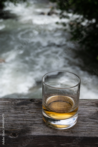 Glass of strong scotch single malt whisky with fast flowing mountain river on background