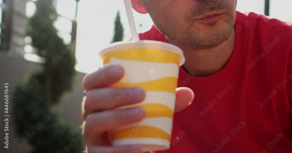 A man with stubble on his face eats French fries and drinks a drink from a paper cup through a pipe against the backdrop of sun. A man with stubble on his face eats French fries and drinks a drink from a paper cup through a pipe against the backdrop of sun.