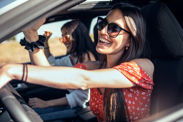 Pretty young women singing while driving a car on road trip on beautiful summer day.