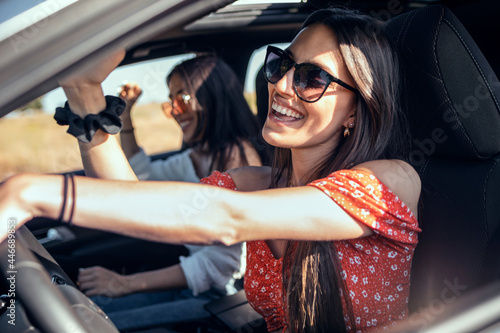 Fototapeta Pretty young women singing while driving a car on road trip on beautiful summer day