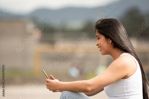 Young latina girl with long hair using a cell phone with the background out of focus.