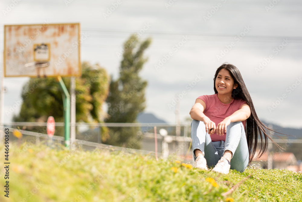 Fototapeta premium smiling Hispanic girl sitting in a green area, relaxation concept