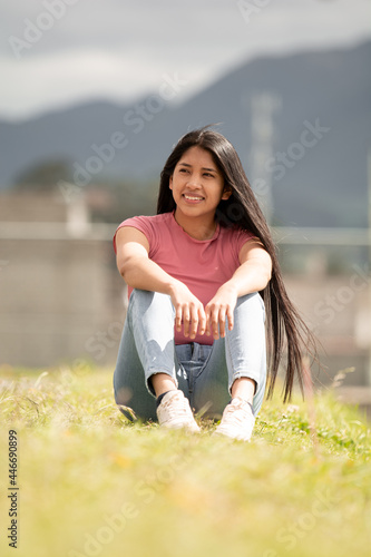 smiling hispanic girl sitting in a green area, concept of freedom
