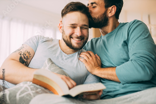 Happy gay couple sitting at home in the morning and reading an exciting book. It takes a little to be happy.