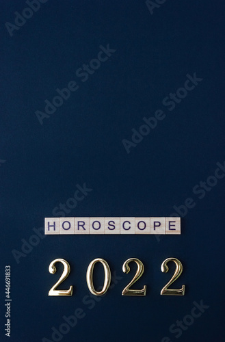 Numbers 2022 and word Horoscope. Wooden blocks with lettering on dark blue background. Vertical poster. Flat lay, copy space