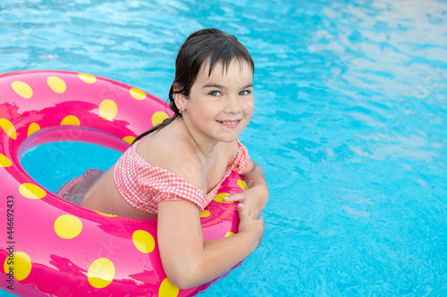 cute smiling girl in a bright circle swims on the background of a blue pool in summer. High quality photo