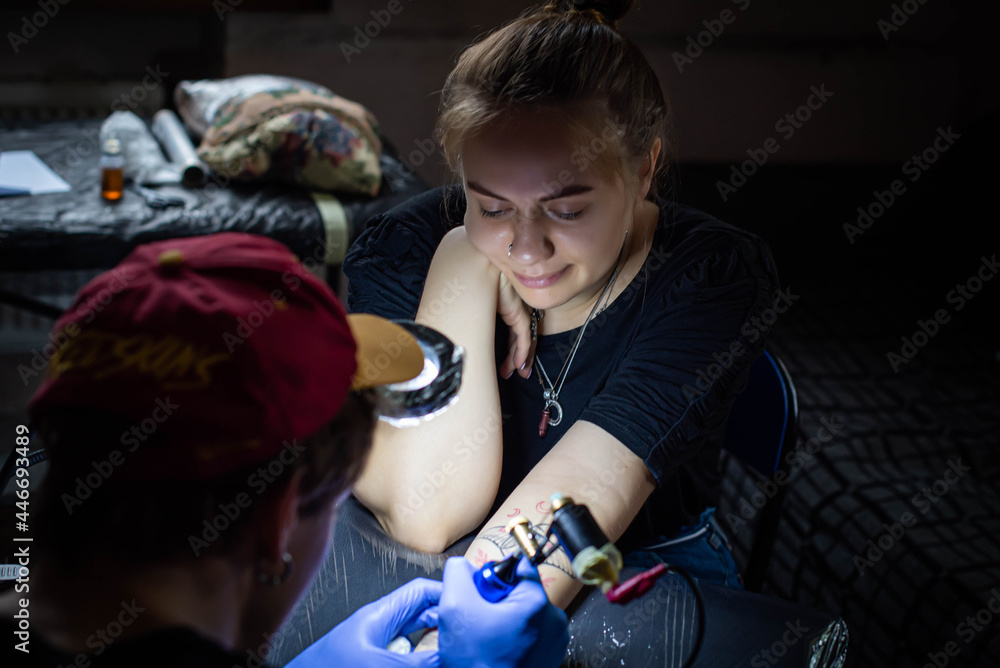 cropped shot of tattooing process on hand in salon. A professional tattoo artist introduces ink into the skin using a needle from a tattoo machine.Professional tattooist working in studio. cropped shot of tattooing process on hand in salon. A professional tattoo artist introduces ink into the skin using a needle from a tattoo machine.Professional tattooist working in studio.