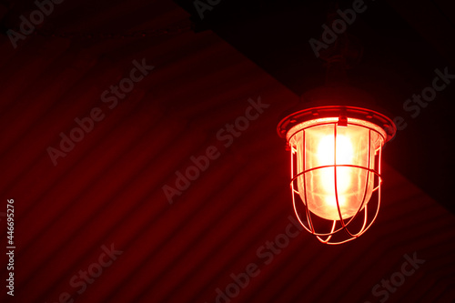 An old signal lamp with red lighting hangs on the ceiling of a room, a building. The lantern creates a semi-darkness