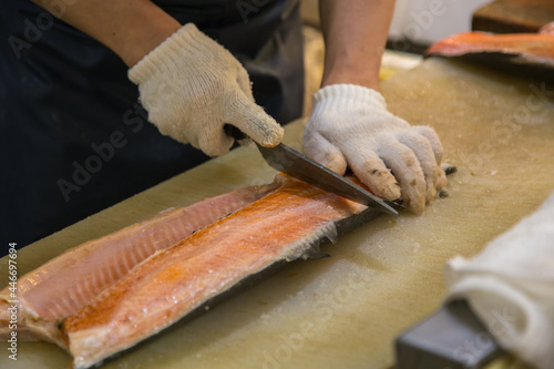 A sushi chef slicing fresh salmon fish , Sushi chef wearing white grove slicing fresh salmon fish