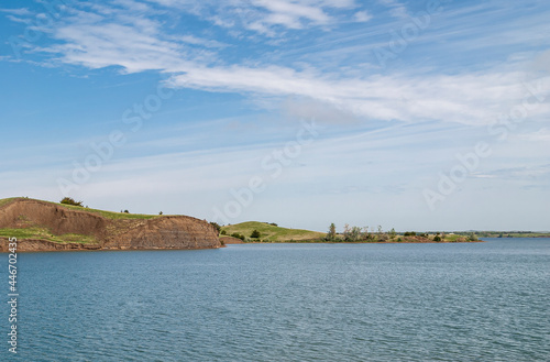 Chamberlain, SD, USA - June 2, 2008: Missouri River North of town. Brown dirt cliff shorline on opposite side of deep blue water under blue cloudscape. Narrow green belt on horizon.