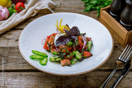 Vegetable salad with tomatoes and cucumbers and red onion and basyl on old wooden table