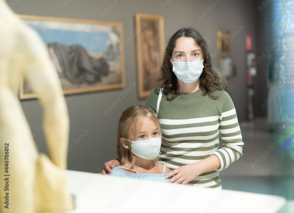 Mother and daughter in protective masks with guide enjoying expositions in museum