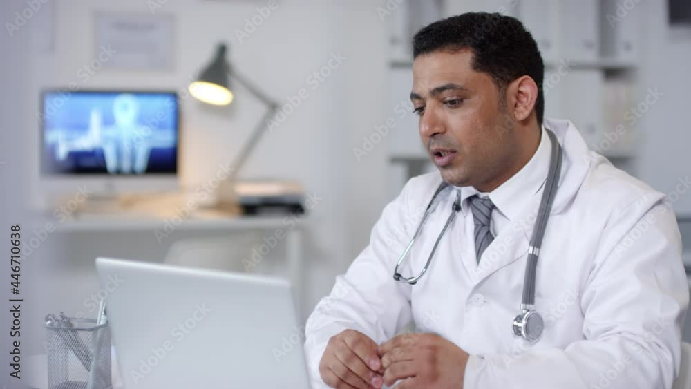 Horizontal medium portrait shot of Middle Eastern general practitioner sitting in his office in front of laptop working with patient on video call Horizontal medium portrait shot of Middle Eastern general practitioner sitting in his office in front of laptop working with patient on video call