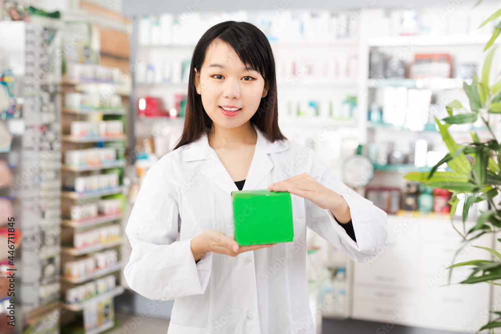Smiling chinese female pharmacist demonstrating assortment of drugstore
