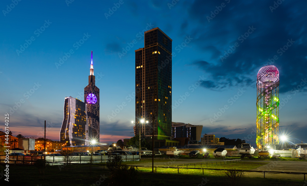 Evening view of Batumi seaside area with lighted modern skyscrapers, Alphabetic Tower, high-rise tower of Technological University and boat parking in foreground