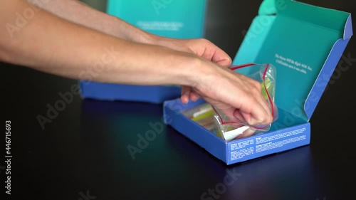 4K clip of woman's hands unpacking contents of a COVID19 home test kit on dark background. Second kit can be seen in background. Pandemic, testing, coronavirus, at home test kit.