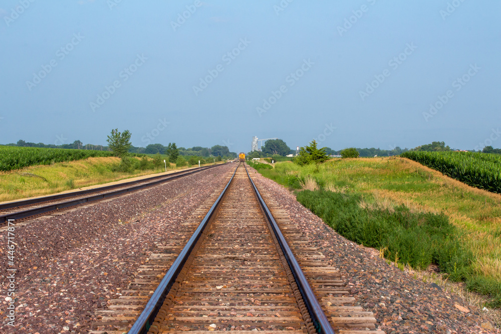 Landscape view of a double railroad track in a rural agricultural landscape on a sunny day, with fields in the background