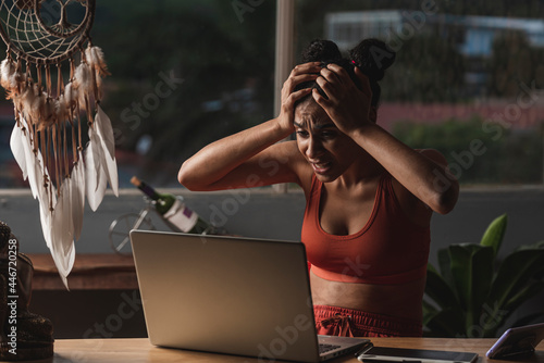 mujer morena sorprendida con las manos en su cabeza y muy asustada con su computadora haciendo tele trabajo  photo