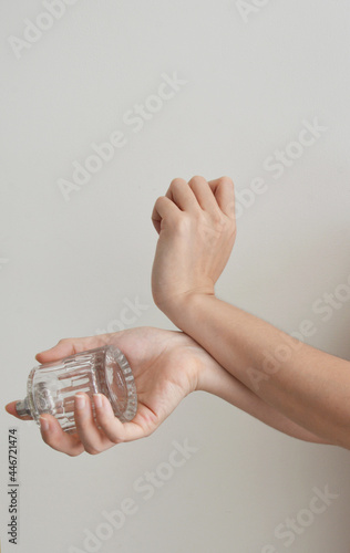 Woman applying perfume to her arm wrist while holding the bottle in white background
