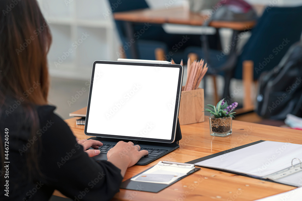 Rear view of businesswoman working on tablet with blank screen while sitting at the table in office. Rear view of businesswoman working on tablet with blank screen while sitting at the table in office.
