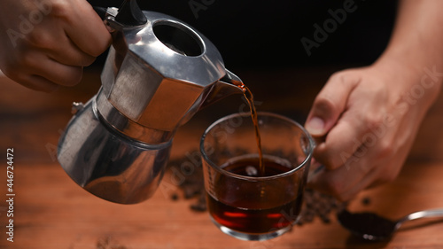 Barista pouring coffee from moka pot into a cup.