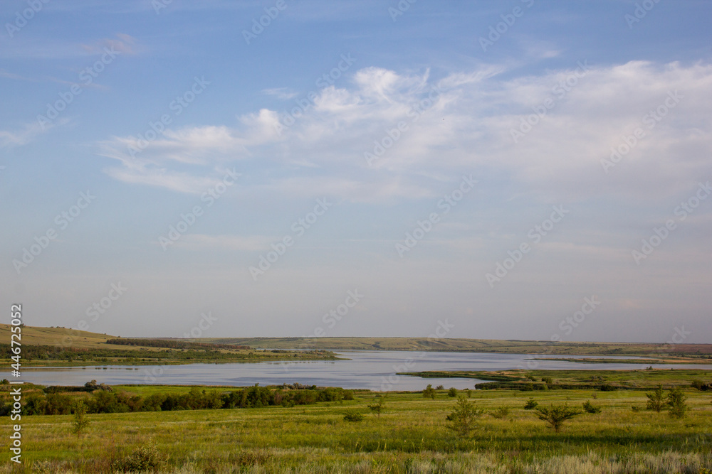 The calm wide river carries its waters under the morning sky. Landscape with hills, trees and a river in Russia