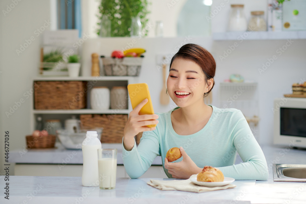 Smiling pretty asian young woman surfing on Internet while having healthy breakfast at home. Smiling pretty asian young woman surfing on Internet while having healthy breakfast at home.