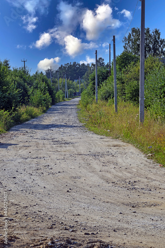 A deserted village road on the background of a blue sky with white clouds