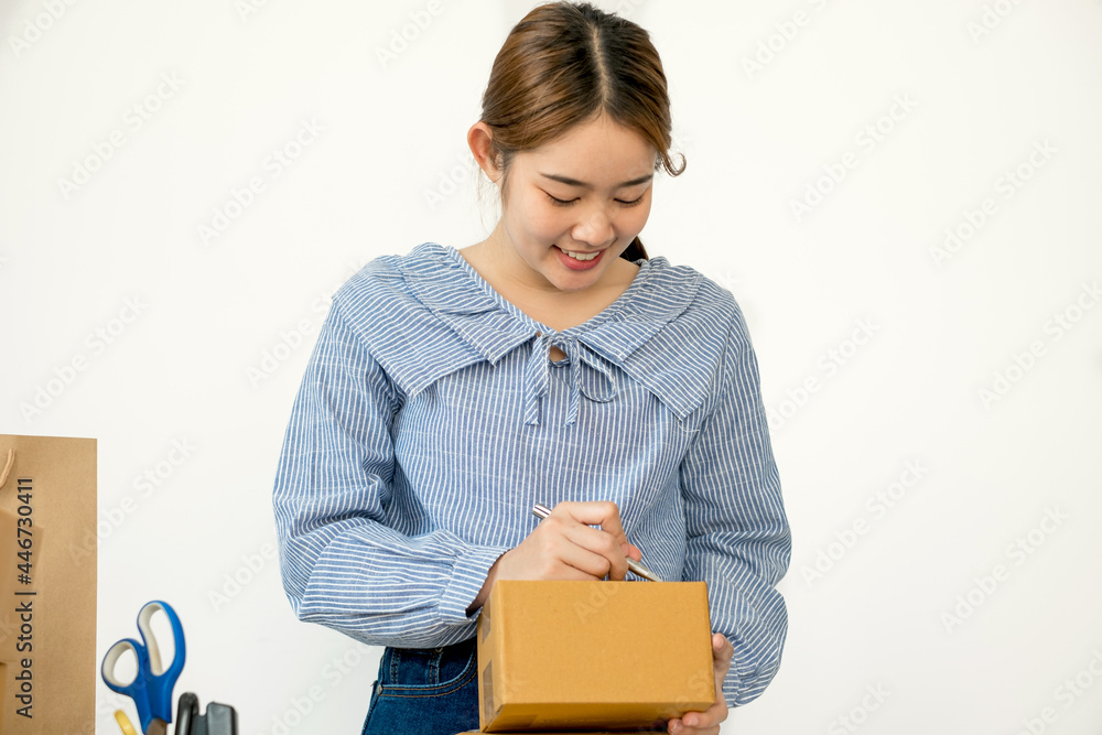 Young Asian woman business owner with many parcel boxes on the table happy online sales job, use the laptop, get an order from customers, take notes, and make arrangements for delivery by post Young Asian woman business owner with many parcel boxes on the table happy online sales job, use the laptop, get an order from customers, take notes, and make arrangements for delivery by post