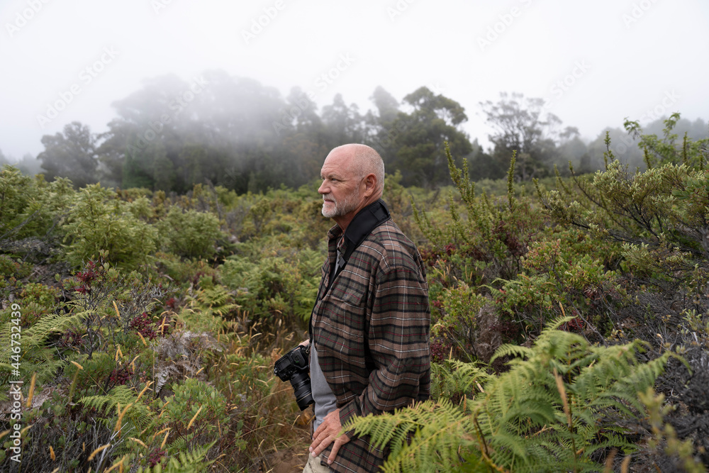 Male senior with a camera enjoying hobby photography outdoors while hiking in a forest