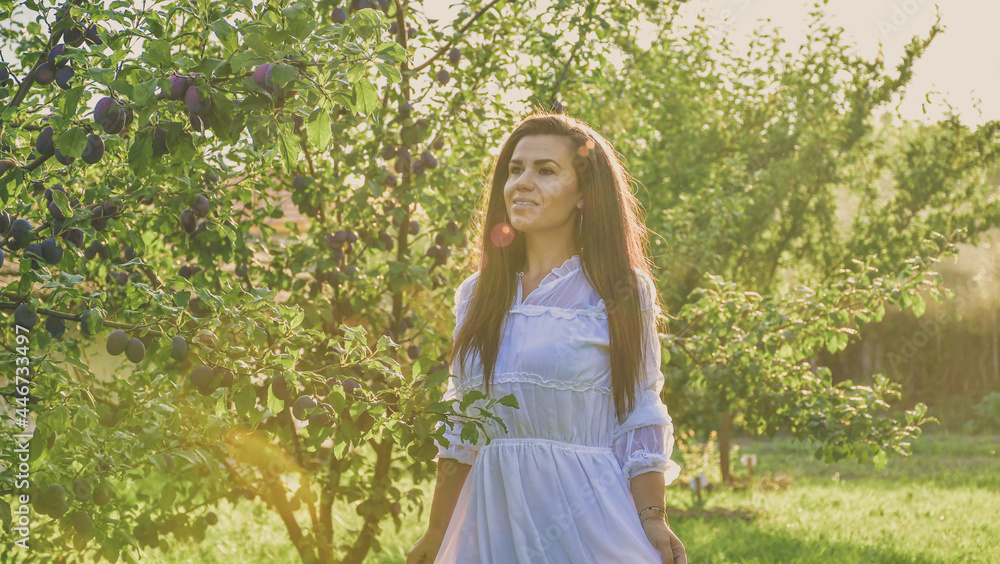 Young beautiful smiling woman with romantic dress at orchar near a plum tree. Young pretty farmer woman Young beautiful smiling woman with romantic dress at orchar near a plum tree. Young pretty farmer woman