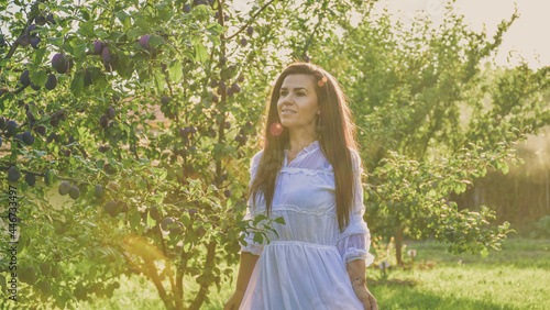 Young beautiful smiling woman with romantic dress at orchar near a plum tree. Young pretty farmer woman