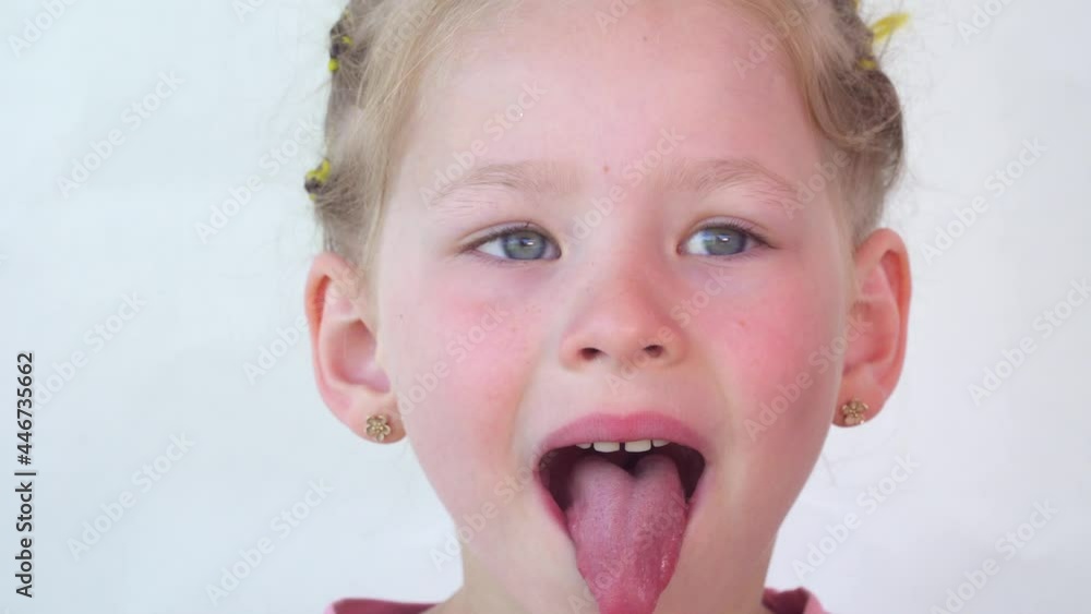 Cheerful child. Girl laughs close-up of the face on a white background. little girl show tongue, throat. portrait with wide open mouth and protruding tongue. with clear view pulls out long tongue. Cheerful child. Girl laughs close-up of the face on a white background. little girl show tongue, throat. portrait with wide open mouth and protruding tongue. with clear view pulls out long tongue.